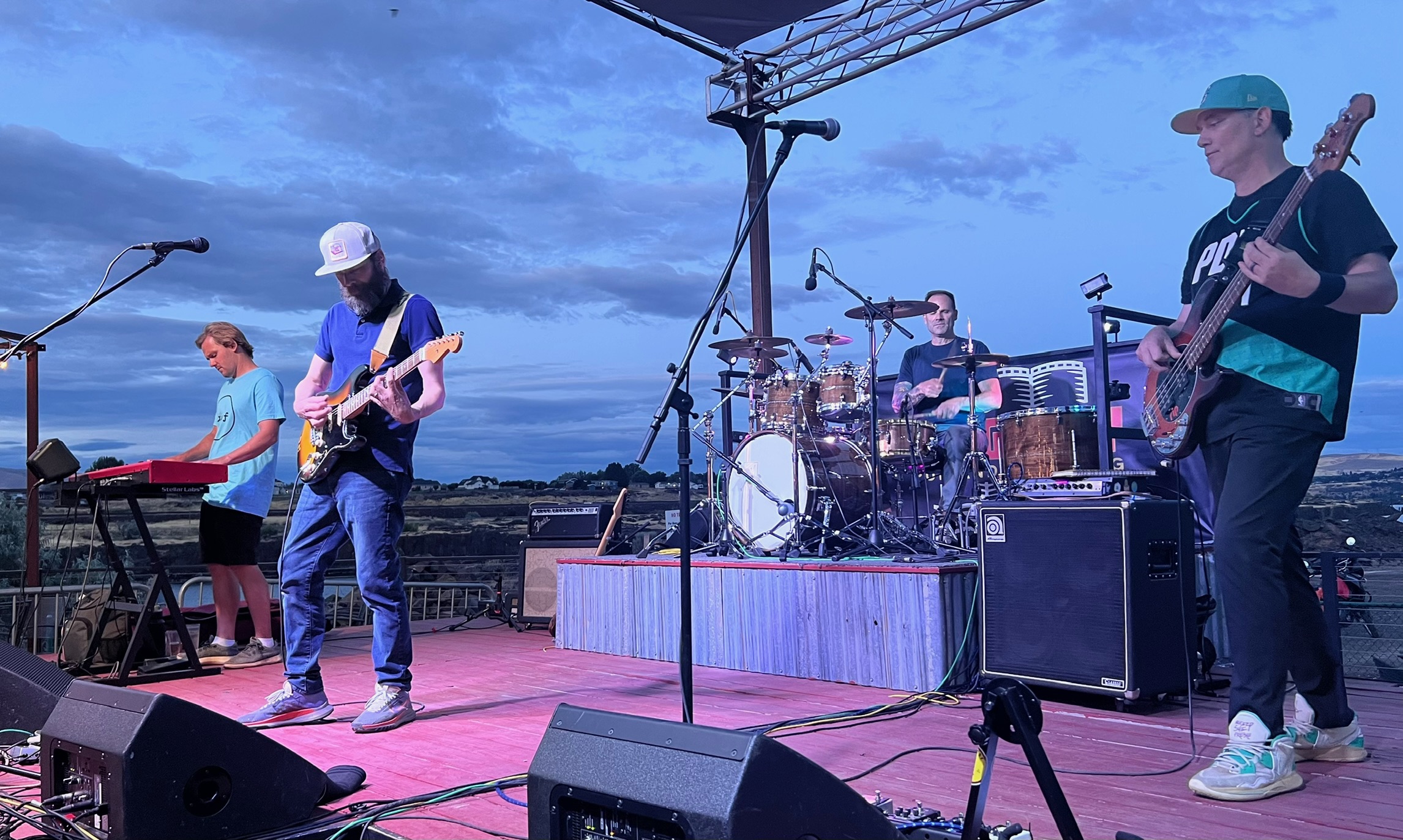 The West Goats on an outdoor stage at dusk, blue sky stretching behind the four-piece band